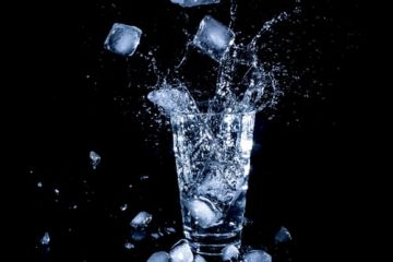 glass-of-water-with-ice-cubes-falling-in-and-splashing-against-black-background