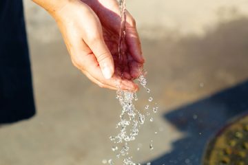 person-cupping-hands-to-catch-stream-of-falling-water-outside