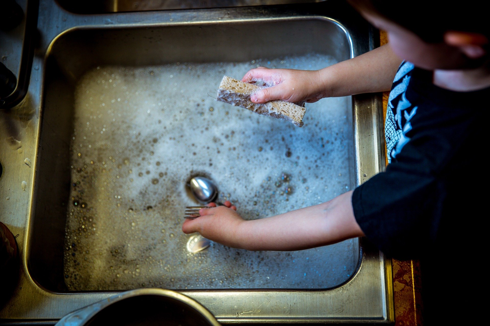 child-washing-dishes-in-sink-filled-with-soapy-water-with-sponge