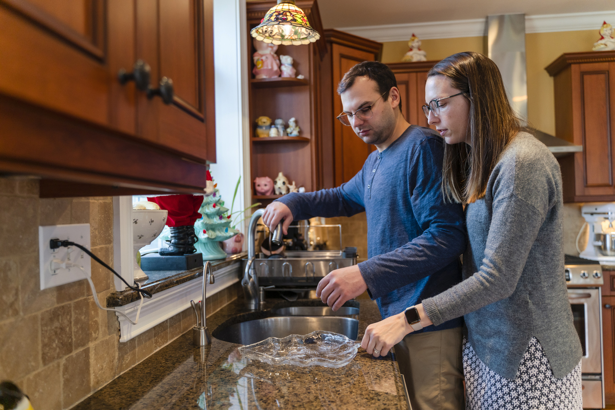 Young couple cleaning dishes in the kitchen after the family dinner and concerned about the hard water in winter weather.